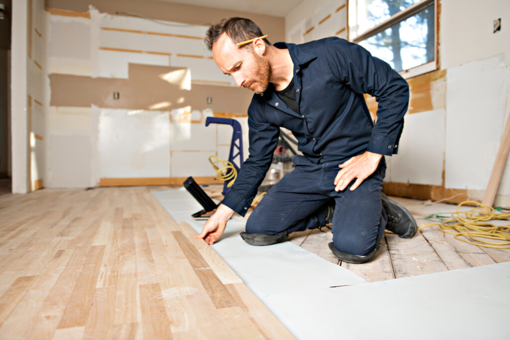 Flooring installer inspecting subfloor moisture barrier before hardwood installation
